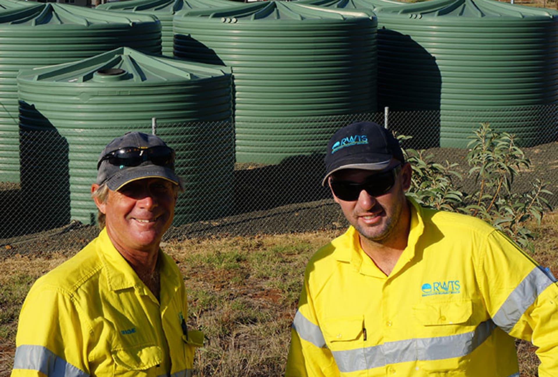 2 service technicians in high vis vests standing in front of green water tanks